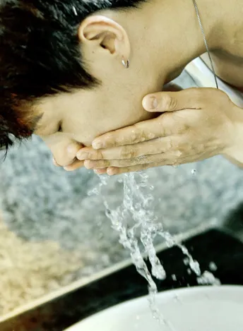 一个年轻人用手在流水下洗脸