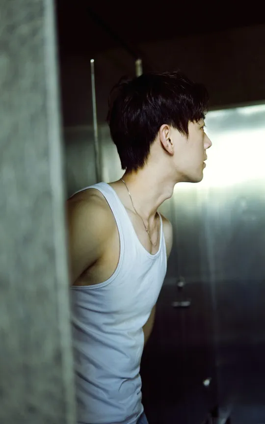 一个穿着白色背心的年轻人站在镜子前