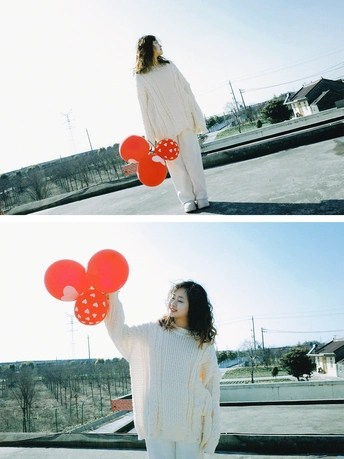 一个穿白色毛衣的女子抱着红气球站在外面
