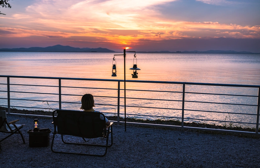 一个人坐在长凳上 观赏着水面上的日落 当太阳在水面上落下。