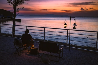 一些人在一个 bench 上搭起的椅子上坐着 俯瞰着夕阳下的水面。