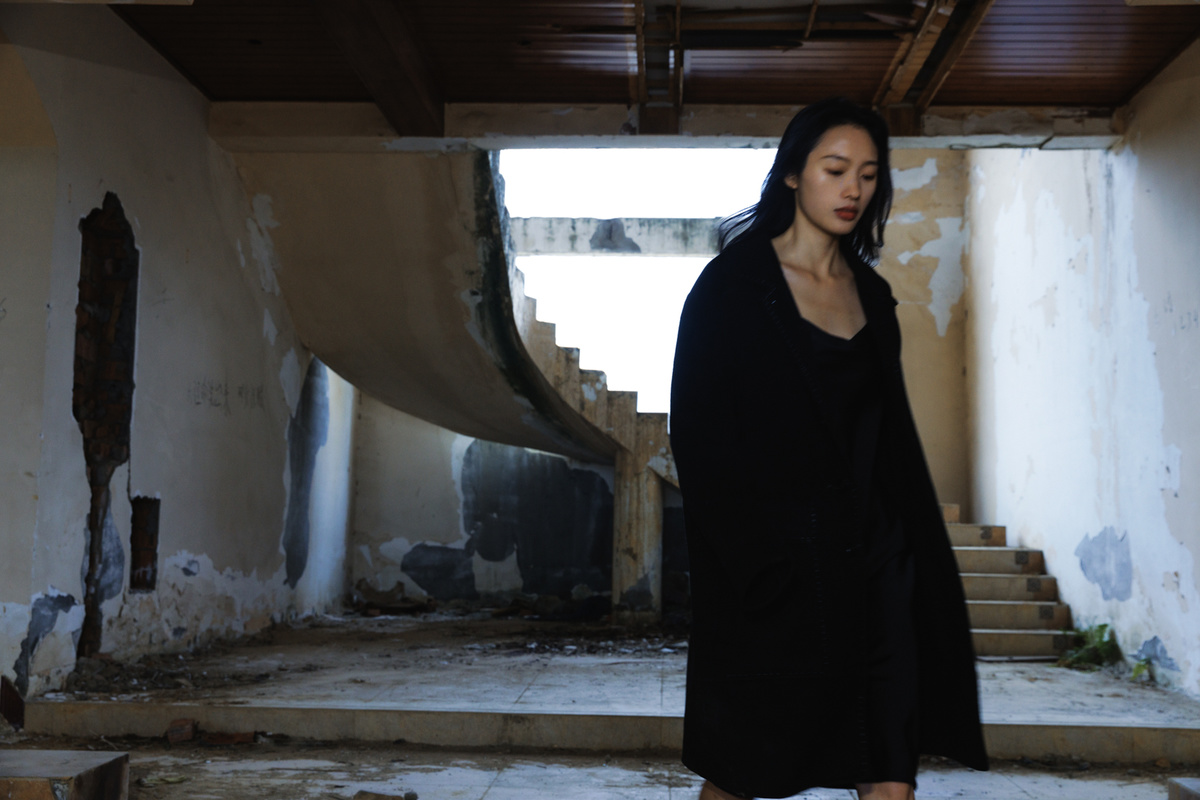一个穿着黑色衣服的女人走下了一个废弃的房子里的楼梯 另一个人站在地板上。