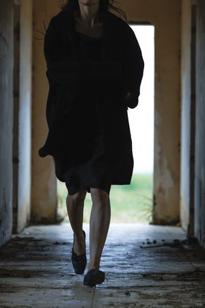 一个穿着黑色连衣裙和外套的女人在一个光线昏暗的废弃建筑物的走廊里走下来。