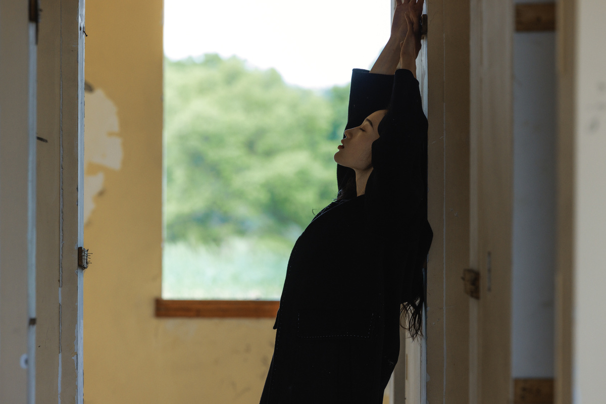 一个女性站在一所房子的走廊里 手里拿着滑板 向外望着窗户。