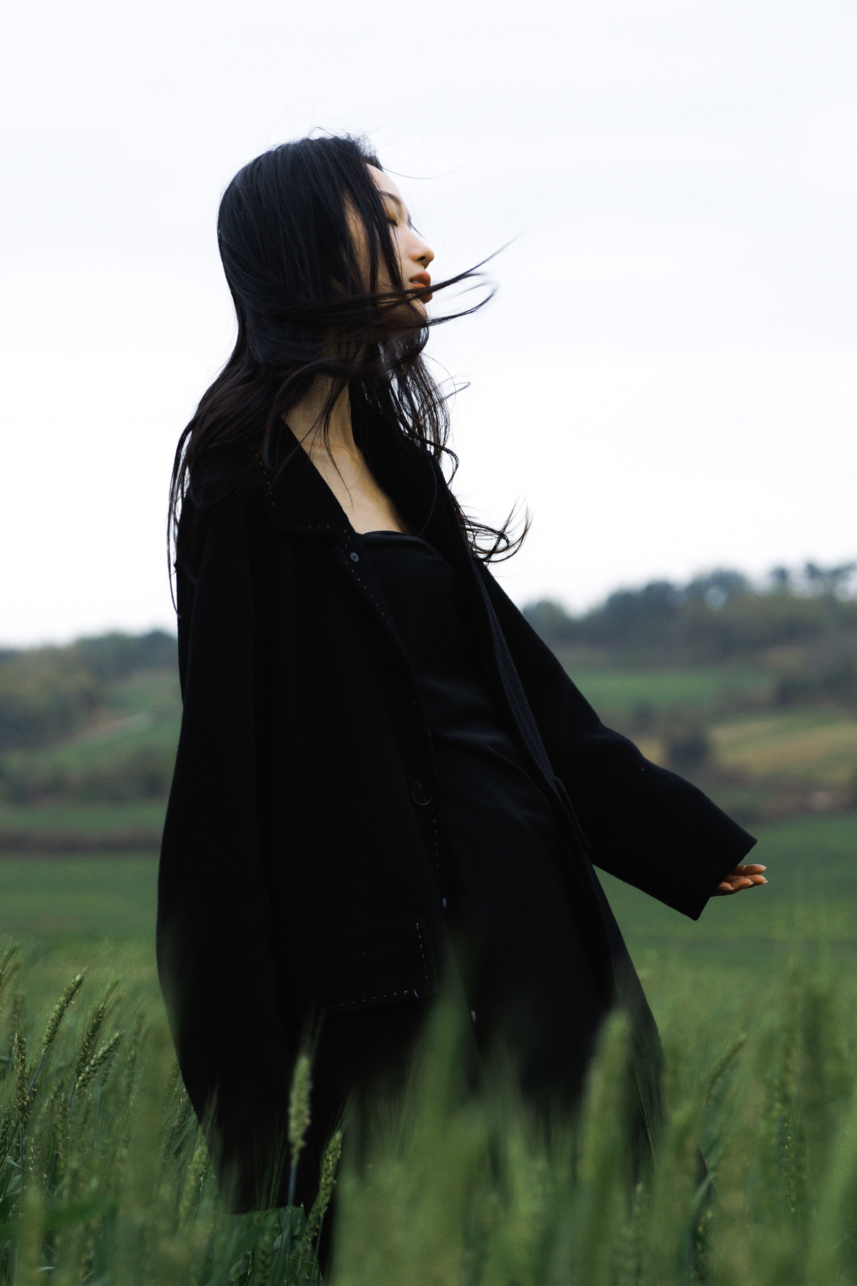一个穿着黑色外套的女人站在绿色的草地上 随风摇曳。