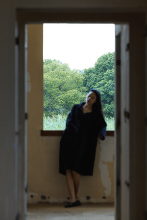 一个披着长袍的女人正在一座建筑物的开着的窗户旁凝视 门口站着一个人。