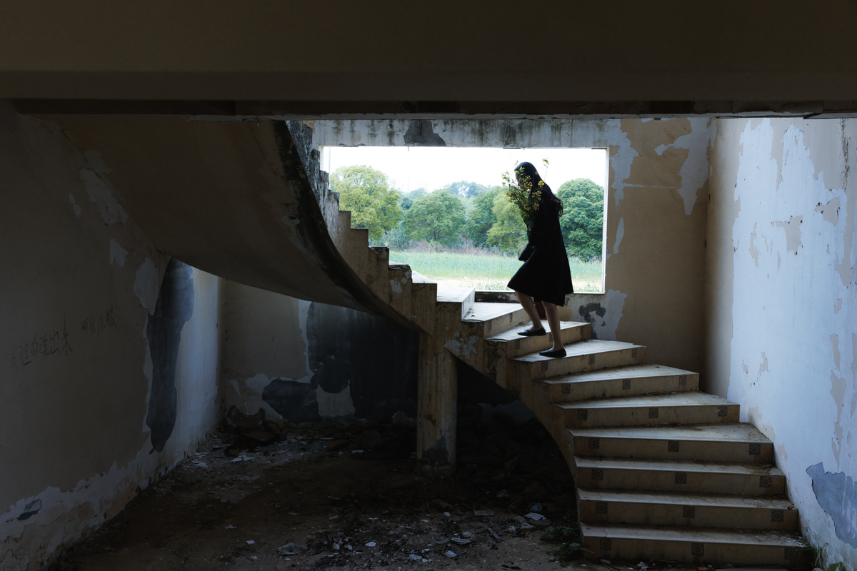 一个穿着连衣裙的女人站在一座废弃的房子里 有人正在走上楼梯。