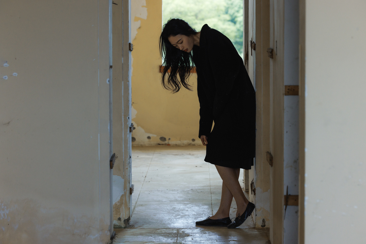 一个穿黑色连衣裙和高跟鞋的女孩走在一条走廊里 朝一个打开的门看去。