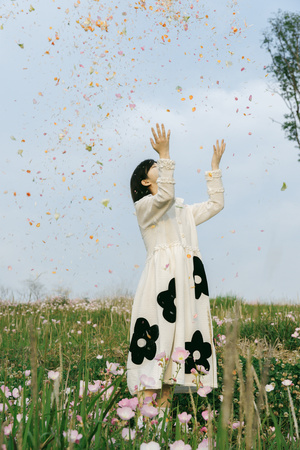 一个穿着裙子的年轻女孩在空中撒满花瓣的田野上举起双手向天空。