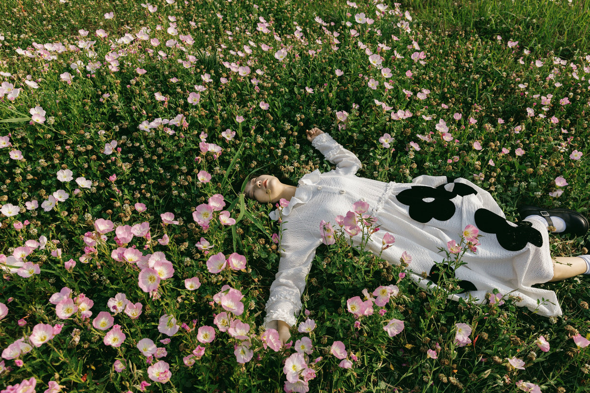 一位 woman 躺在草地上的一朵花床上 上面躺着一头 cow。