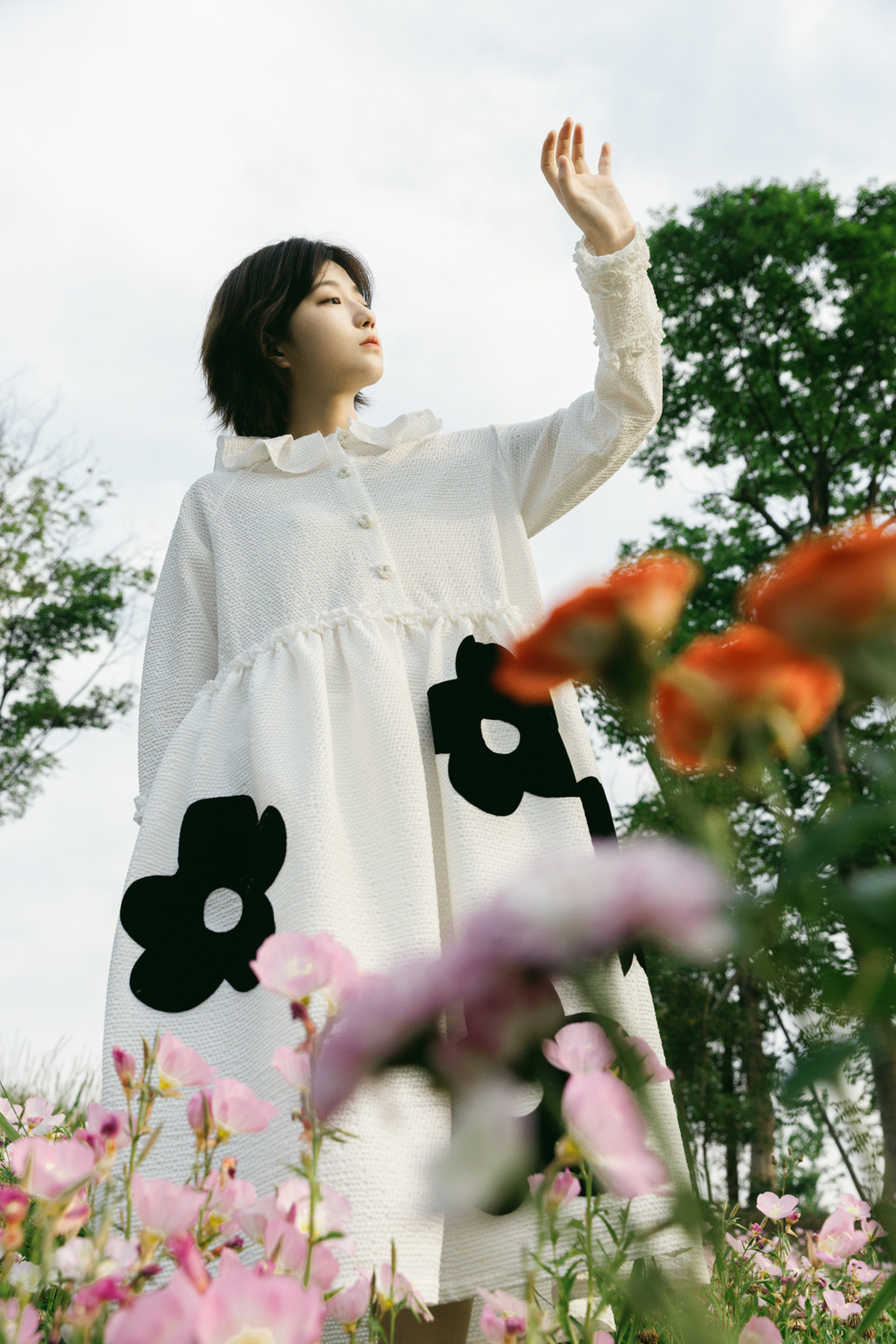 一个穿着白色连衣裙的年轻女子站在花田里 双手举向天空。