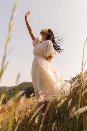 一个穿着白色连衣裙的年轻女子站在一个草地上 双手伸向天空。