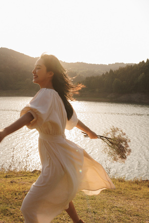 一位穿着白色连衣裙的年轻女子手里拿着飞盘沿着湖边走