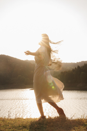 夕阳下在湖边穿白裙跳舞的年轻女子