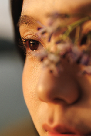 一位年轻女子用双手捂住鼻子 将一朵紫色花举到眼前
