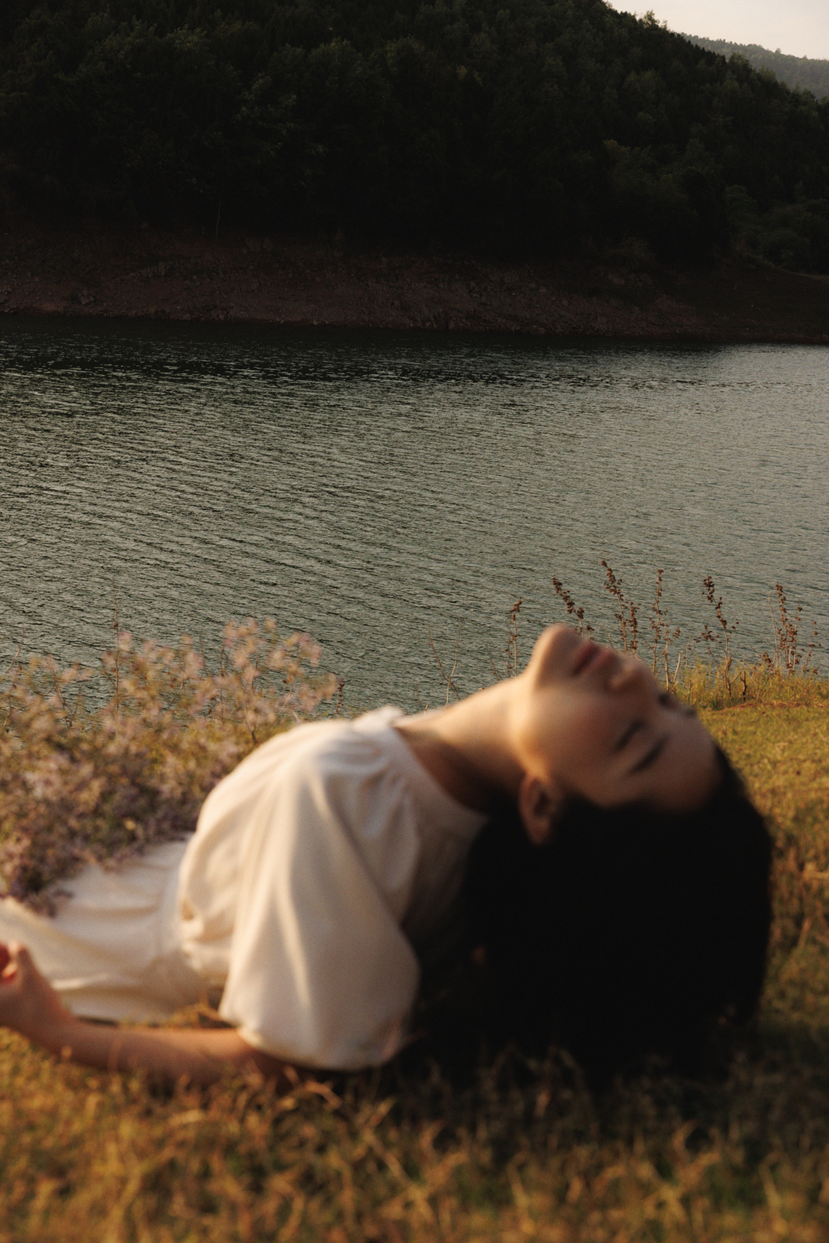 一位穿着白色的年轻女子躺在草地上 靠近水域或湖泊。