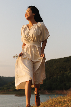 一位穿着白色连衣裙站在湖边小山上的女人 背景中有水。