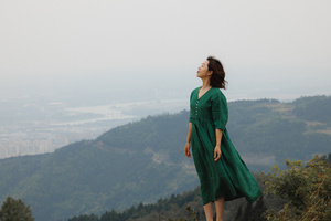 一位穿着绿色连衣裙的女人站在山顶 俯瞰着山谷和城市。