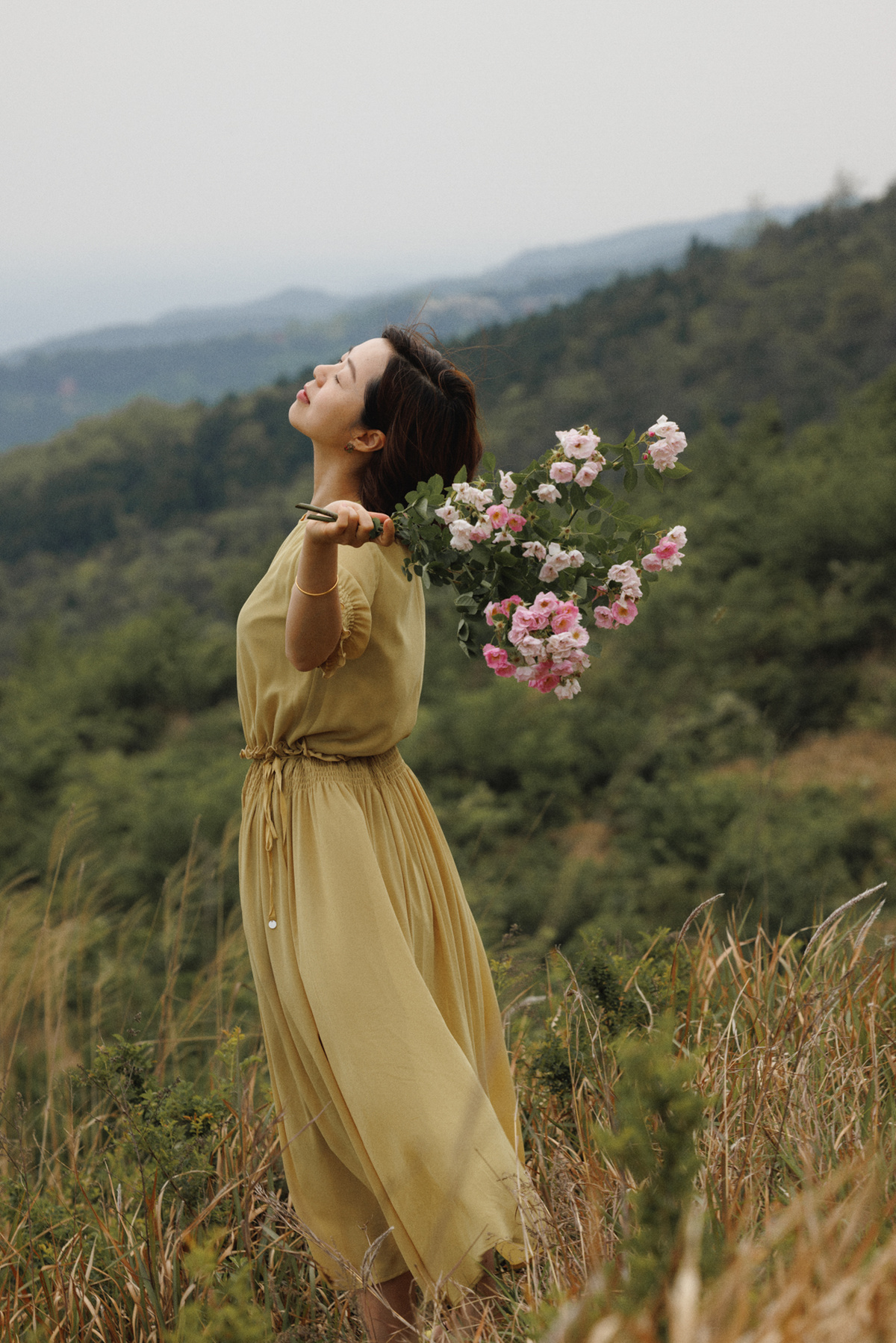 一位穿着黄裙子的年轻女子在田地里嗅着花。