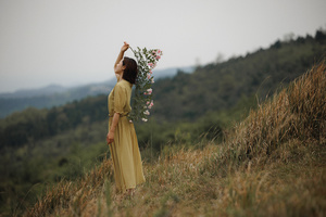 站在山丘上的一个穿着黄色连衣裙的年轻女子手拿一束花