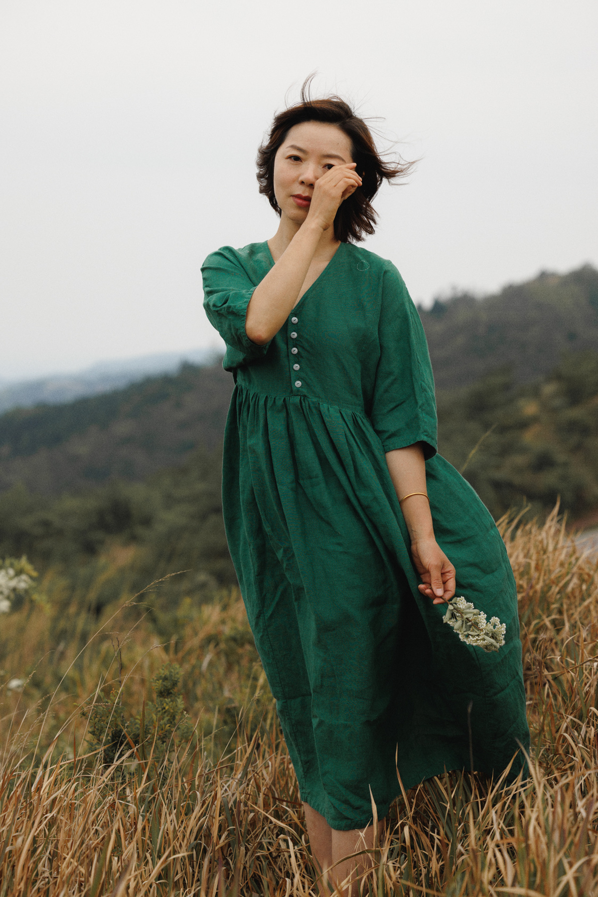 一位穿着绿色连衣裙的女士站在一片高草丛中