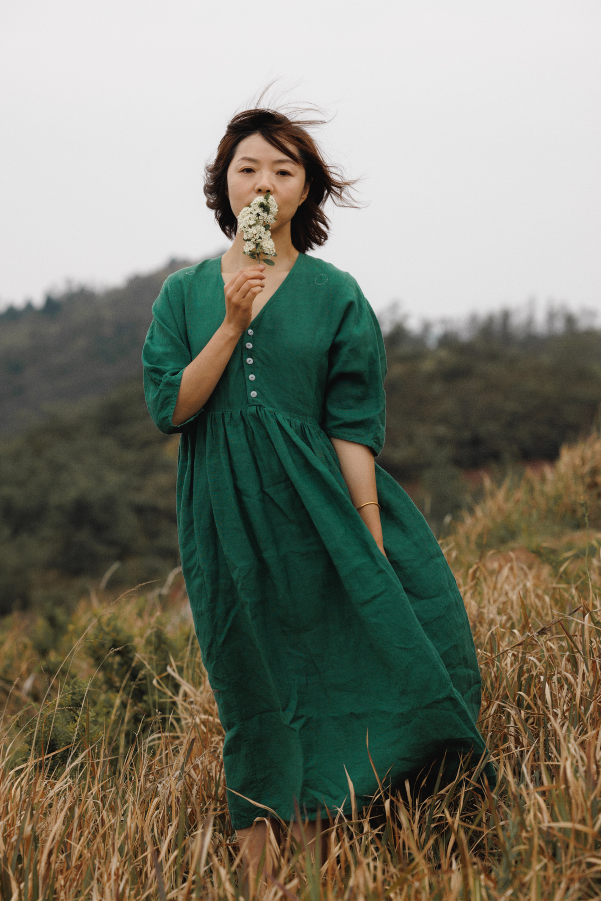 一位穿着绿色连衣裙的年轻女子正在田地里吃一朵花。