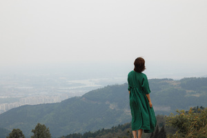 一位穿着绿色连衣裙的女士站在山顶 俯瞰着山谷和城市。