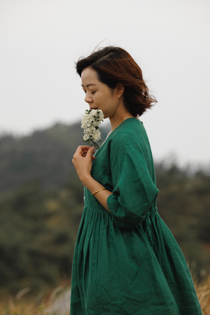 一位穿着绿色连衣裙的年轻女子在田野中闻着白色花朵的香气。