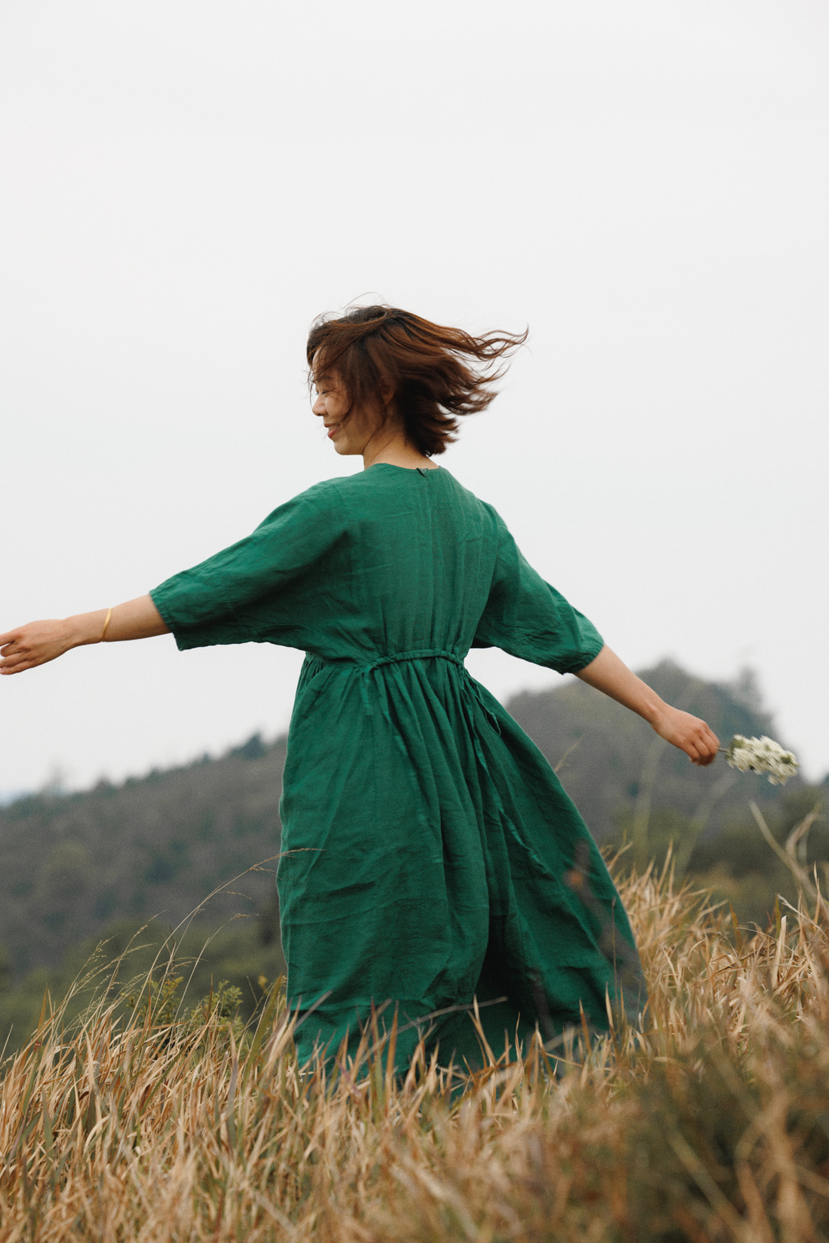 一个穿着绿色连衣裙的年轻女子 在茂密的草地上奔跑 双手伸开 手里拿着一个飞盘。