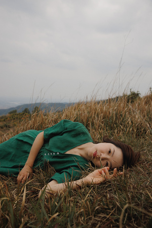 一位穿着绿裙子的年轻女子躺在山丘上的 tall grass 中。
