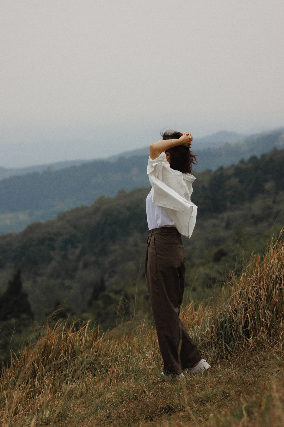 一位穿着白衬衫的女士站在一个绿草丛生的小山丘的顶部。