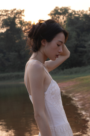 一位美丽的年轻女士穿着白色连衣裙站在靠近水域或河流的地方