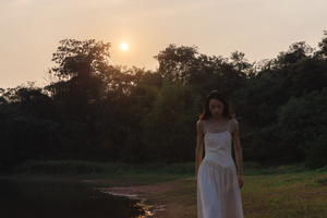 一位穿着白裙子的年轻女子站在田野中 当太阳落山时 河面上的景色变得美丽。