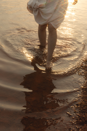 一个穿着白裙子的年轻女孩站在浅水中 太阳在海洋中照耀着她。