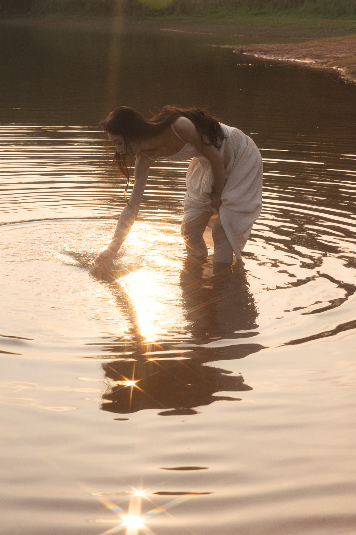 一位穿着白色衣服的年轻女子站在一个水域中