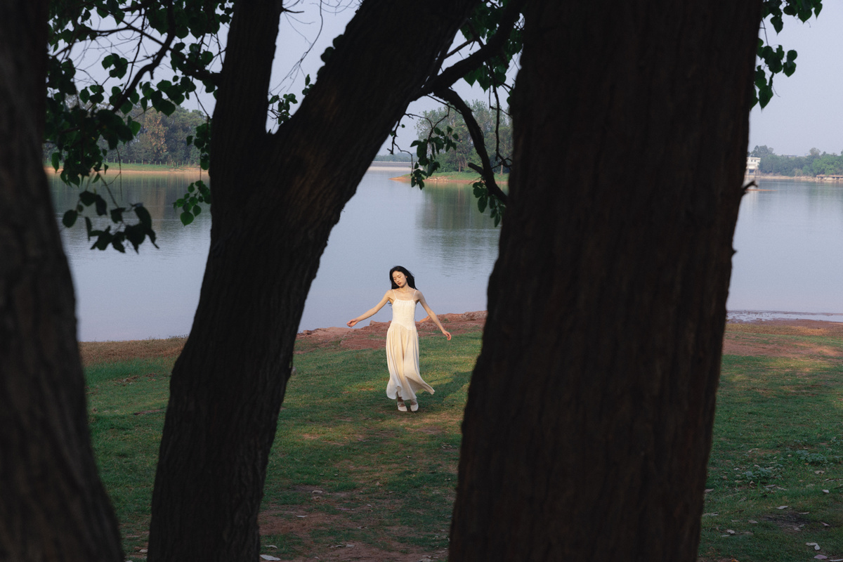 一位穿着白色连衣裙的年轻女子穿过一个靠水的公园。