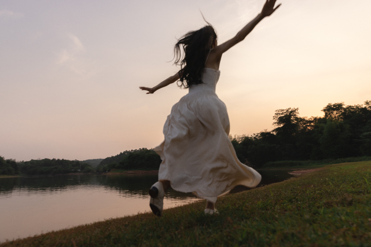 一个穿着白裙子的年轻女子在日落时分在水上跳一个飞盘。