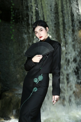 一位穿着黑色和服的女性拿着扇子站在瀑布前摆姿势