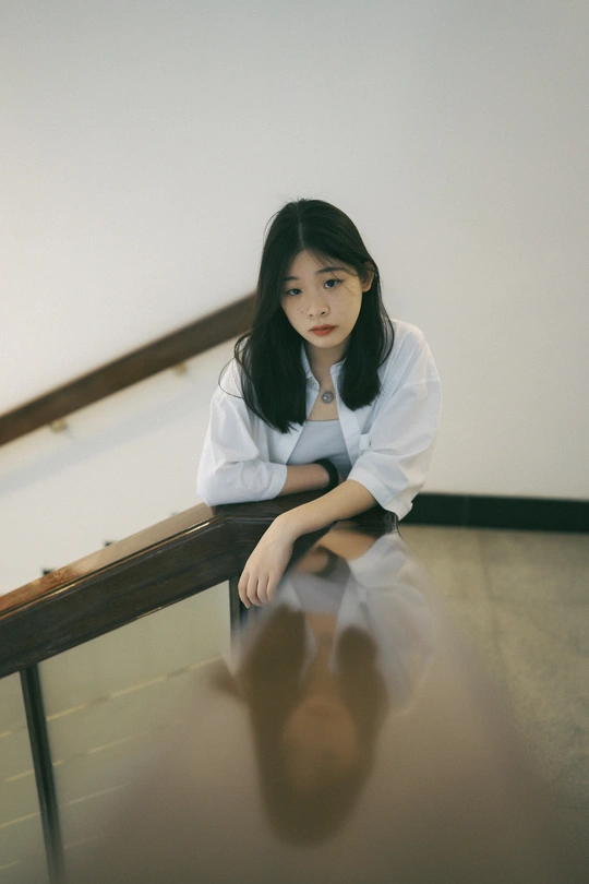 一个穿着白衬衫的年轻女子坐在地板上 旁边有栏杆。