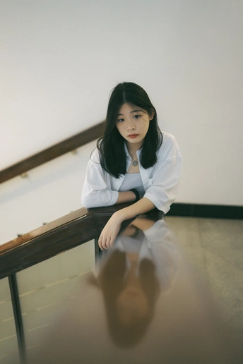 一个穿着白衬衫的年轻女子坐在地板上 旁边有栏杆。