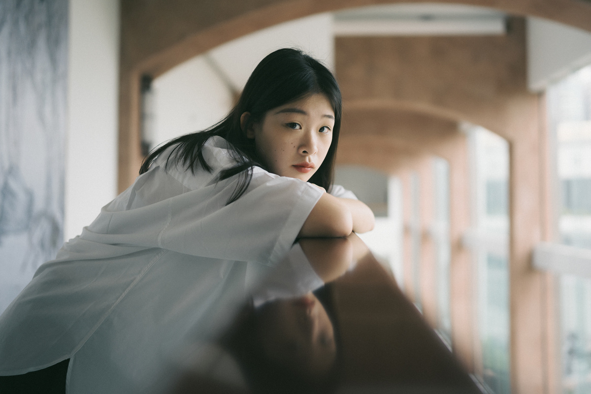一位穿着白色衬衫的年轻女子坐在窗前