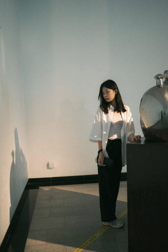 一位穿着白衬衫的年轻女子靠在一间有雕塑的房间的墙上