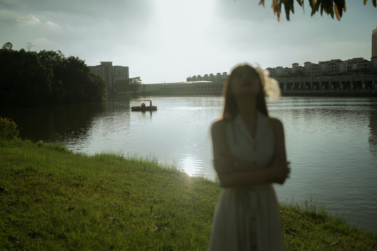 一位穿着白色连衣裙的年轻女子站在靠近水域的地方 太阳落山了。