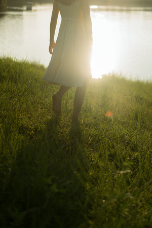一个穿着白裙子的年轻女子站在日落时的田野中 太阳照亮了水面。