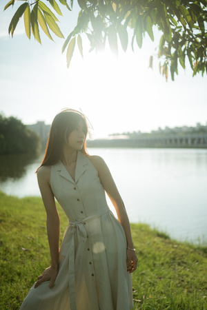 一位穿着白色连衣裙的年轻女子站在一个有树木和草地的湖边田野上