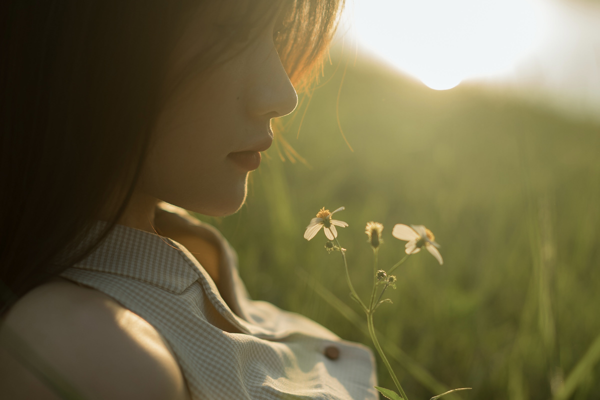 一位年轻女子坐在草地上凝视着一朵白色花朵