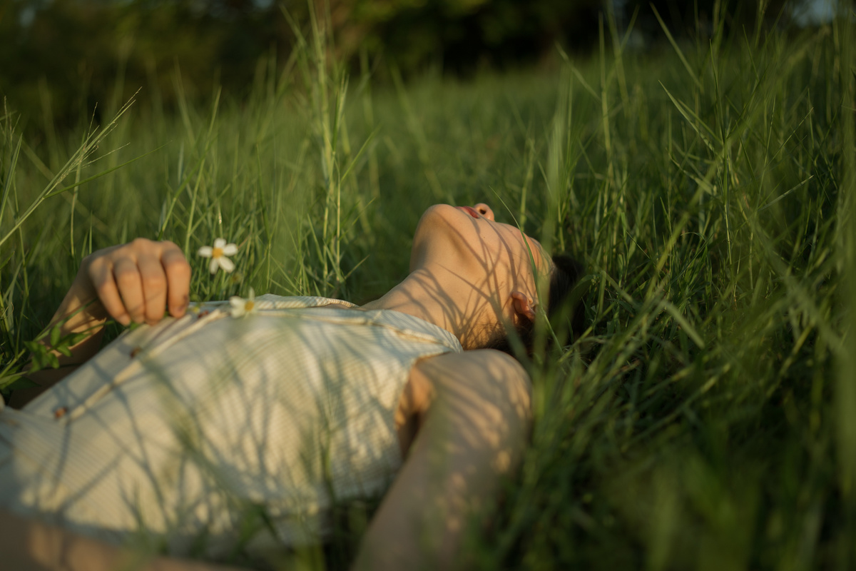 一位年轻女子躺在长满野草的草地上 地上有一朵花。