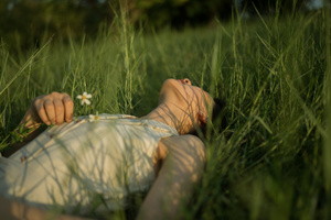 一位年轻女子躺在长满野草的草地上 地上有一朵花。