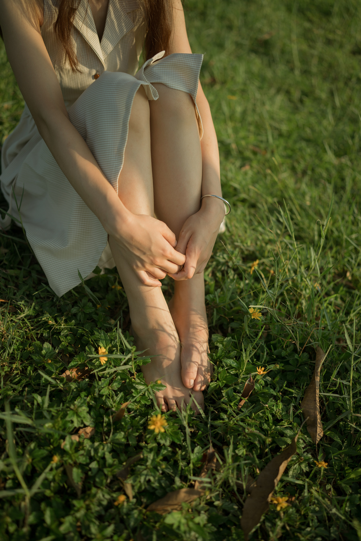 一个穿着白色裙子的年轻女子坐在绿色的草地上 双手放在膝盖上