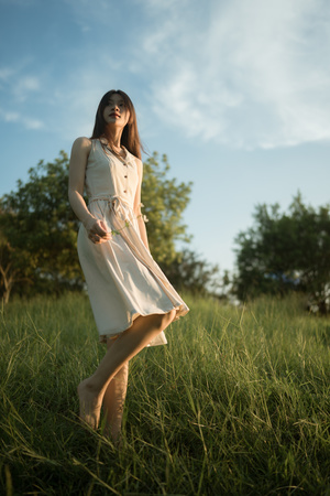 一位穿着白色连衣裙的年轻女子穿过草丛茂密的草地 走进草地上空旷的田野。